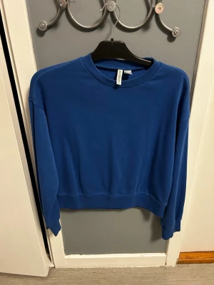 Blå sweatshirt från H&M - En enkel blå sweatshirt från H&M med rund halsringning och ribbade muddar vid ärmslut och nederkant. Tröjan passar mig som är 155 och kan säkert passa någon som är längre. Använt typ 1 en gång!