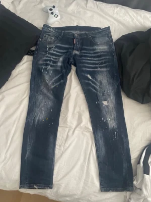 Mörkblå dsquared2 jeans med färgstänk - Säljer ett par mörkblå jeans med slitningar, färgstänk och tvättade detaljer. Jag är 175 cm och väger 64kg och sista bilden motsvarar hur dem sitter på mig.