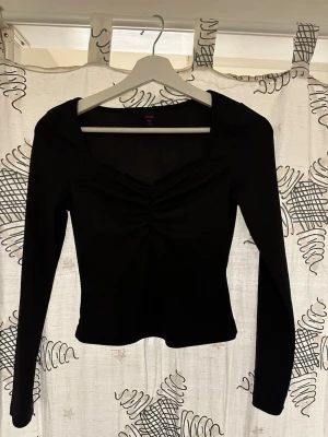 Svart långärmad topp från Romwe - Trendig svart långärmad topp från Romwe i ribbad stretchig polyester. Toppen har en snygg rynkning framtill och en smickrande v-ringad urringning. Perfekt att styla med jeans eller kjol för en cool look.