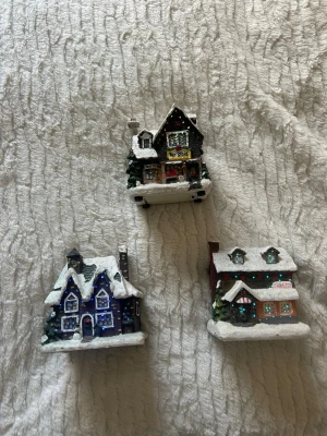 Miniatyrhus med snö, 3-pack - Tre små dekorativa miniatyrhus i olika färger med snötäckta tak och detaljer som granar och skyltar. Husen  passar perfekt som pynt till vintern eller julen. Blinkar i olika färger 