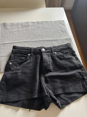 Svarta shorts från H&M, storlek 38 - Säljer ett par svarta shorts från H&M i storlek 38. De har klassisk design med knapp och dragkedja framtill, och är tillverkade i ett bomullsmaterial som känns bekvämt och snyggt. Perfekta för dig som vill ha ett enkelt och stilrent plagg till sommaren.
