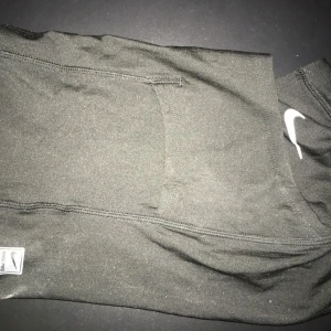 Svart Nike ski-mask - Säljer ett svart ski-mask från Nike med en diskret ficka på sidan och vit Nike-logga. Tillverkade i stretchigt och mjukt material som passar perfekt till träning eller chill. Snygga sömmar och klassisk design.