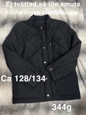 Svart quiltad jacka med dragkedja - Stilren svart quiltad jacka med hög krage och tryckknappar framtill. Jackan har en bröstficka med dragkedja och två sidofickor. Passar perfekt till vardags och har en klassisk look.🌸 Finns inte någon storlekslapp men uppskattar till 128/134. Ej tvättad så lite smuts kvar.