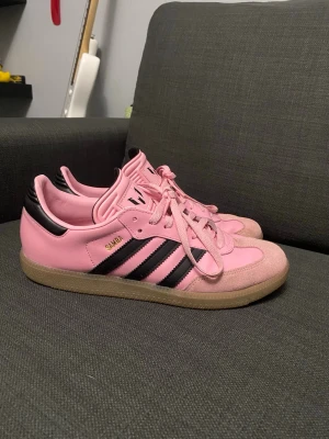 Adidas Samba rosa sneakers - Säljer ett par Adidas Samba sneakers i rosa med svarta detaljer, (Messi Miami). Köpt förra sommaren, säljer då de inte används. 