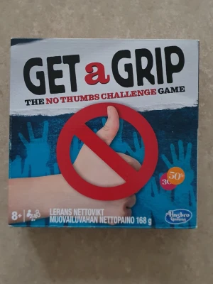 Get a Grip - The No Thumbs Challenge Game - Get a Grip är ett roligt och utmanande sällskapsspel där du ska klara uppgifter utan att använda tummarna. Spelet kommer i en färgglad kartong och innehåller spelkort, tummband och modellera. Perfekt för att utmana vänner och familj med kreativa och knasiga uppdrag.