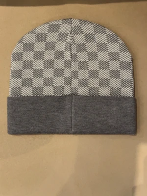 Grå rutmönstrad mössa - Snygg mössa med grå  rutigt mönster och enfärgad grå uppvikt kant. Perfekt accessoar för att hålla värmen och ge din outfit en cool touch. Tillverkad i mjukt stickat material som känns skönt mot huden.