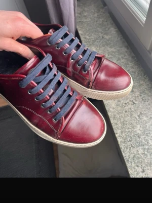 Lanvins  - Snygga vinröda sneakers i läder-look med mörkblå snören och vit sula. Klassisk låg modell med rund tå och diskreta sömmar. Perfekta för dig som vill ha en stilren och enkel sneaker med lite färg. Passar till både jeans och chinos. Har små slitningar men inget som märks 