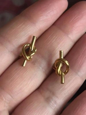 knutörhängen i stål metall - Snygga örhängen i guldfärgad stål metall med unik knutdesign. Perfekta för dig som gillar minimalistiska och trendiga accessoarer. Stiftmodell som sitter bekvämt på örat och ger en cool touch till din stil. Liknar Sophie by Sophie knot serie smycken 