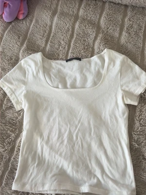 Vit topp med fyrkantig ringning Brandy Melville - Vit kortärmad topp från Brandy Melville med snygg fyrkantig ringning. T-shirten är i mjuk bomull och har en enkel, clean look som passar till allt. Perfekt för dig som gillar minimalistisk stil och vill ha en basic topp i garderoben.