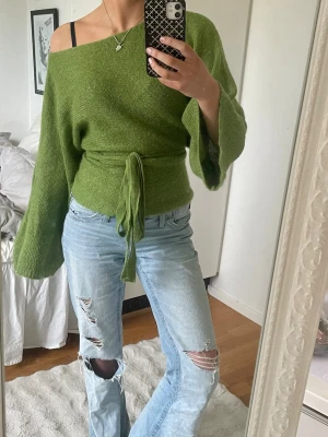 Grön unik  stickad tröja - Snygg grön stickad tröja med unik-design och vida ärmar. Tröjan har ett knytband i midjan som ger en markerad siluett. Perfekt för dig som gillar en avslappnad men trendig stil. Kan bytas på flera sätt