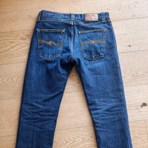 Mörkblå jeans från Nudie Jeans(big Bengt) - Modellen big Bengt, 28/32! Det är inte smuts vid knät utan ljus kontrasten! Snygga mörkblå jeans från Nudie Jeans med klassisk femficksdesign och kontrastsömmar. Jeansen har raka ben och detaljerade bakfickor med Nudie-loggan broderad. Tillverkade i slitstark denim av bomull.