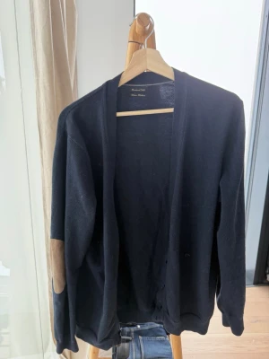 Mörkblå cardigan  - Stilren mörkblå cardigan från Massimo dutti med knäppning framtill och snygga mockadetaljer på armbågarna. Perfekt för lager på lager och har en klassisk, avslappnad passform. Tillverkad i mjukt material som känns skönt mot huden. Cashmere o merinoullblanding