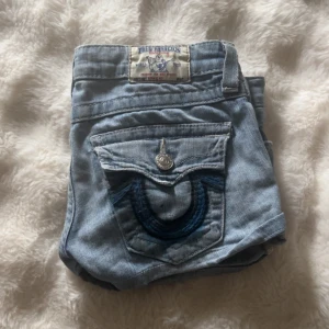 Low waist  Vintage truereligionshorts one of a kind  - Säljer ett par ljusblå jeansshorts från True Religion med klassiska kontrastsömmar och dekorativ ficka bak. Shortsen har låg midja, knappgylf och detaljer i silverfärg. Perfekta för sommardagar och har en avslappnad passform.