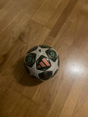 Adidas fotboll Champions League - Säljer en Adidas fotboll med Champions League-design. Bollen har ett mönster med vita, svarta och turkosa stjärnor samt Adidas-logga i orange. Tillverkad i slitstarkt syntetmaterial och perfekt för spel på gräs eller konstgräs.