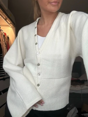Vit ribbad kofta med knappar - Stilren vit kofta med v-ringning och silvriga knappar framtill. Från Gina, använd fåtal gånger 