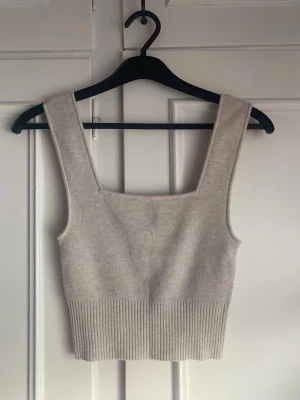 Beige stickat/ribbat linne - Säljer ett beige stickat linne med breda axelband och fyrkantig ringning. Toppen är ribbad nedtill och har en enkel och stilren design som är lätt att matcha. Använd fåtal gånger, inga tecken på användning.💕☀️