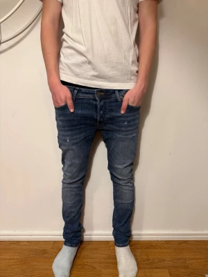 Blå slim fit jeans med slitningar från jack&jones  - Säljer ett par blå slim fit jeans med lätt slitna detaljer och tvättade partier. Jeansen har klassisk femficksmodell, knappgylf och smal passform. Perfekta för en avslappnad och trendig look. W30 L30