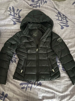 Svart dunjacka med huva från ROCKANDBLUE - Oanvänd svart dunjacka från Rockandblue med huva och två dragkedjeförsedda fickor framtill. Pälsen saknas.