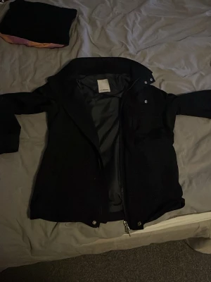 J lindeberg fieldjacket  - Stilren svart jacka från J.Lindeberg med dragkedja och hög krage. Jackan har en minimalistisk design och är tillverkad i ett slätt material som känns bekvämt. Perfekt för dig som gillar klassisk och enkel stil.