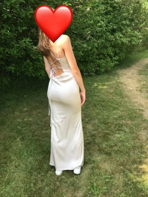 Champagne färgad satinklänning med snörning - Balklänning i satin med öppen rygg och snygg snörning bak. Använd en gång så i jättebra skick. Från Nelly i storlek 38, men går att reglera bak i ryggen hur man vill att den ska sitta.