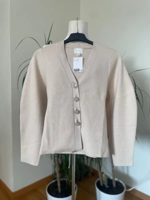 Beige kofta med dekorativa knappar - Stilren beige kofta med v-ringning helt ny med lappar på 
