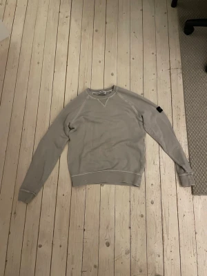 Beige sweatshirt från Stone Island - Snygg beige sweatshirt från Stone Island Junior med klassisk rund halsringning och ribbade muddar. Tröjan har en diskret patch på ärmen och är tillverkad i mjuk bomull för maximal komfort. Perfekt för en avslappnad och stilren look.