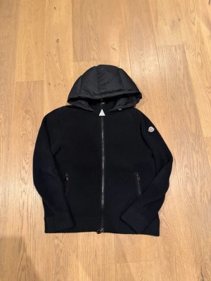 Moncler cardigan  - Svart cardiganjacka från Moncler med stickade ärmar och framstycke samt quiltad, vadderad rygg och huva. Dragkedja framtill och två fickor med dragkedja. Moncler-logga på vänster ärm. Perfekt nu för våren. Hör av er vid eventuella frågor! 🤩