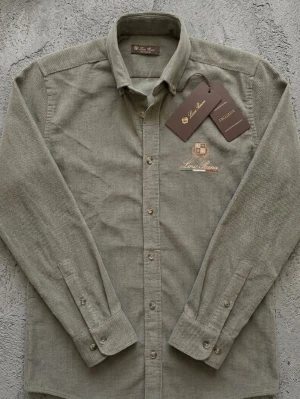 Grå manchesterskjorta från Lord Guano - Stilren grå skjorta i manchester från Lord Guano med broderad logga på bröstet. Skjortan har klassisk krage, knäppning framtill och långa ärmar med manschettknappar. Perfekt för dig som gillar en tidlös look.