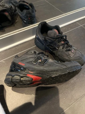 Svarta New Balance 1906R sneakers - Säljer ett par svarta New Balance 1906R sneakers med detaljer i rött och silver. Skorna har en chunky sula, mesh och syntetmaterial i ovandelen samt klassisk N-logga på sidan. Grymma för dig som gillar sportig och modern stil.i storlek 39 vi kan diskutera om vi kan byta