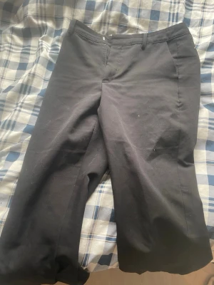 Svarta kostymbyxor - Snygga svarta kostymbyxor med raka ben och klassisk passform. Byxorna har hällor för bälte, diskreta fickor bak och är gjorda i ett slätt material som känns bekvämt. Perfekta för dig som vill ha en stilren look.