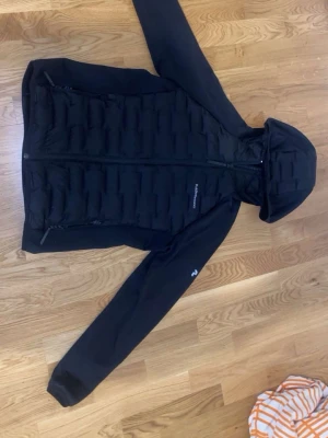 Svart dunjacka Peak Performance XL - Säljer en svart dunjacka från Peak Performance i storlek XL passar även man S. Jackan har huva, dragkedja framtill och två sidofickor med dragkedja. Snygg quiltad design på framsidan och ärmar i mjukare material. Perfekt för kalla vinterdagar.
