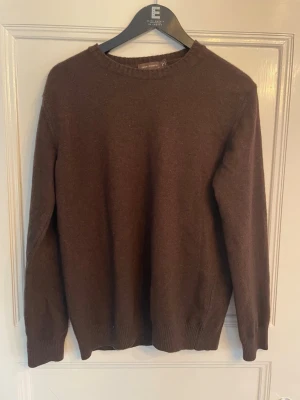 Brun <<Oscar Jacobson>> stickad tröja - Mjuk och stilren brun stickad tröja från Oscar Jacobson. Tröjan har rund halsringning, långa ärmar och ribbade muddar vid ärmslut och nederkant. Perfekt för lager på lager och enkel att matcha med olika outfits.