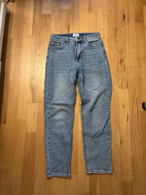 Blå raka jeans från ONLY - Säljer ett par klassiska blå jeans från ONLY med rak passform och hög midja. Jeansen har fem fickor, bälteshällor och stängs med knapp och dragkedja. Tillverkade i ett slitstarkt denimtyg som ger en tidlös look.
