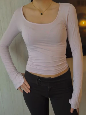 Ljusrosa långärmad topp - Säljer en ljusrosa långärmad topp med tight passform och bred, rundad urringning. Toppen är enkel och stilren, perfekt att matcha med olika outfits. Materialet känns mjukt och stretchigt, vilket gör den bekväm att bära.