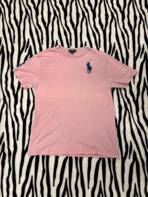 Ralph Lauren t-shirt  - Snygg rosa t-shirt från Ralph Lauren med blå logga på bröstet och en blå 3 på ärmen. Tröjan väldigt go nu till varmare tider! Storlek är i barn XL (18-20år) men i vuxen blir det S, den är rätt stor så S-M! Hör av dig vid minsta fundering 🤙