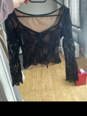 Svart spetsblus med snörning - Säljer en svart, transparent spetsblus med långa ärmar och snygg snörning framtill. Blusen har v-ringad urringning och croppad passform, perfekt för att lyfta vilken outfit som helst. Bilderna är från min vinted sida. 🥰