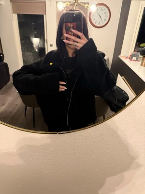 Svart teddyjacka med dragkedja - Mysig svart teddyjacka med oversized passform och dragkedja framtill. Jackan har bred krage och långa ärmar, perfekt för att hålla värmen. 