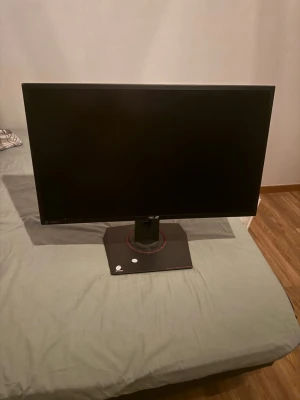 ASUS gaming skärm 24 tum - Säljer en svart ASUS gaming skärm med stilren design och stabil fot. Skärmen har tunna kanter och en rund röd detalj på foten. Perfekt för gaming eller arbete, kopplas enkelt till datorn via HDMI eller DisplayPort.