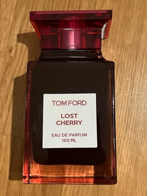 Tom Ford Lost Cherry EdP 100 ml - Tom Ford Lost Cherry Eau de Parfum 100 ml är en lyxig parfym i en elegant mörkröd glasflaska med matchande kartong. Doften är känd för sina söta och fruktiga körsbärstoner och flaskan har en modern, fyrkantig form med en stilren etikett. Fått i present, aldrig använd. 