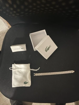 Silverfärgat armband från Lacoste - Snyggt silverfärgat armband från Lacoste med stilren länkdesign. Armbandet kommer med original ask och tygpåse med Lacoste-logga. Perfekt accessoar för dig som gillar klassisk och sportig stil.