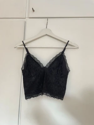 Svart spetslinnetopp  - Snygg svart linnetopp med spetsdetaljer och smala axelband från BikBok. Toppen har v-ringad hals och spetskant både upptill och nedtill. Perfekt att styla till festen eller sommarkväll.