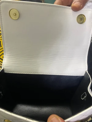 Vit quiltad handväska med gulddetaljer - Snygg vit handväska i quiltat mönster med guldfärgade magnetlås. Väskan har en klassisk rektangulär form och är tillverkad i konstläder. Perfekt för dig som gillar stilrena accessoarer med en lyxig touch.