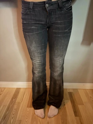 Mörkgrå bootcut jeans från weekday  - Säljer ett par mörkgrå bootcut jeans från weekday med snygga slitningar och klassisk femficksmodell. Jeansen har låg midja och utsvängda ben, vilket ger en retro och avslappnad look. Materialet är mjukt denim med stretch för extra komfort. Jeansen är använda ca 4 gånger 