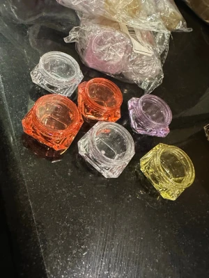 Färgade tomma burkar för nageldekoration - Säljer flera små tomma burkar i plast för förvaring av nageldekorationer, glitter eller pulver. Burkarna är fyrkantiga och finns i olika färger som orange, gul, lila och transparent. Perfekt för att organisera nagelpyssel och hålla ordning på småsaker. Totalt 31 stycken 