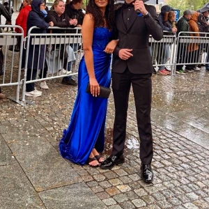 Blå långklänning med paljettdetaljer - Säljer en elegant blå långklänning med glittriga paljettdetaljer upptill och figurnära passform. Klänningen har en axelbandslös design och ett lätt släp. Perfekt för bal eller festliga tillfällen. Matcha med en clutch för en komplett look.