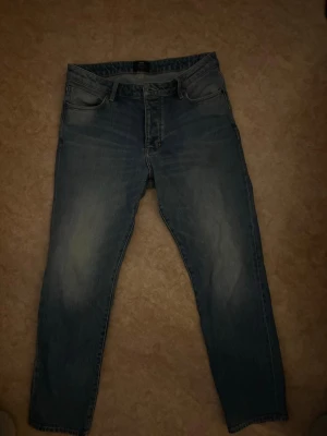 Blå jeans från Neuw med tvättad look - Säljer ett par blå jeans från Neuw med snyggt tvättad look och raka ben. Klassisk femficksmodell med knappgylf och subtila slitningar på låren. Perfekta för dig som gillar en avslappnad men stilren vibe.