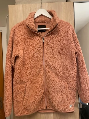 Rosa teddyjacka  - Mysig rosa teddyjacka från lager 157 med dragkedja framtill och två fickor. Jackan har hög krage och är gjord i fluffigt teddy-material som håller dig varm. Perfekt för dig som gillar en avslappnad och trendig stil.