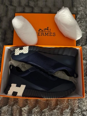 Mörkblå H sneakers med vit detalj - Snygga mörkblå sneakers från H med stickad ovandel och coola vita detaljer på sulan. Skorna har en chunky sula och en låg silhuett som ger en modern vibe. Perfekta för dig som vill ha något exklusivt och trendigt i garderoben.