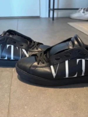 Svarta Valentino sneakers - Snygga svarta sneakers från Valentino med  vit logga på sidan. Skorna har lågt skaft, svarta skosnören och är tillverkade i slätt läder. Knappt använda, min kille köpte en annan färg han gillade bättre. Öppen för bud! 