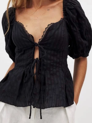 Svart blus med puffärm från NA-KD - Trendig svart blus från NA-KD med puffärmar, v-ringning och spetsdetaljer vid urringningen. Blusen har knyt framtill och lätt utsvängd passform. Perfekt för dig som vill ha en feminin och chic topp med snygga detaljer.